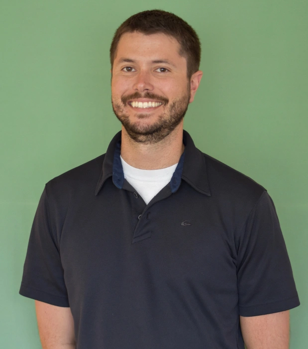 Professional headshot of smiling man in dark polo shirt against green background.